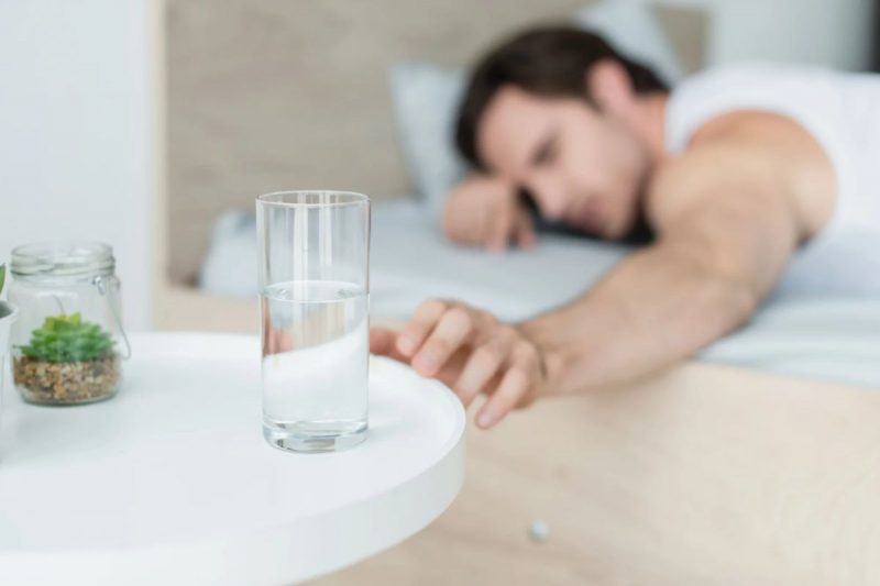 homem colocando um copo de água com sal em cima da mesa de cabeceira ao lado da cama antes de dormir 