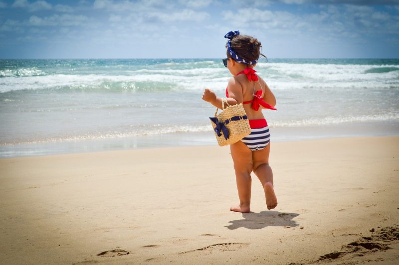 bebê caminhando na areia em direção ao mar da praia 