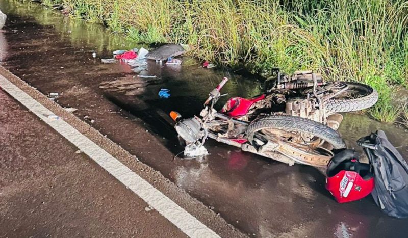 Criança de 12 anos dirigia uma das motocicletas e ficou em estado grave, foto mostra motocicleta vermelha caída no acostamento do asfalto e com ferragens torcidas