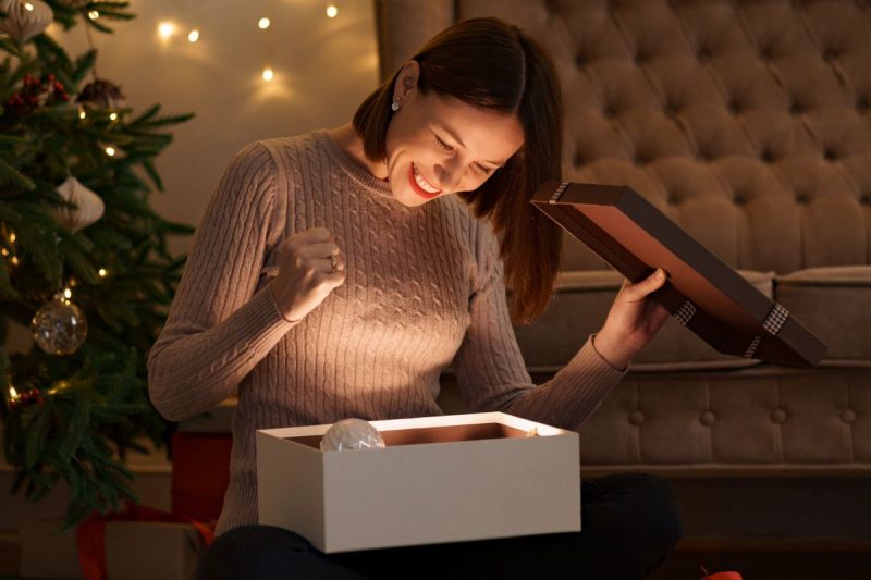 mulher sorrindo olhando presente de natal na frente da árvore