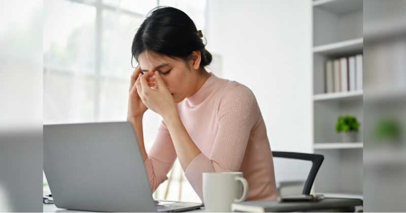 Pessoa com dedos no rosto em frente a computador 