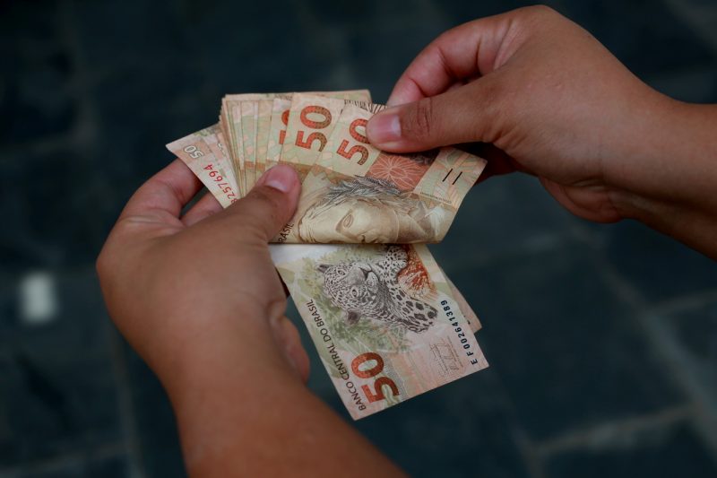 Foto de mãos com notas de R$50 que representa famílias catarinenses endividadas