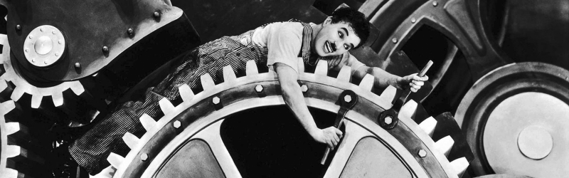 Charles Chaplin deitado em uma engrenagem no filme Tempos Modernos