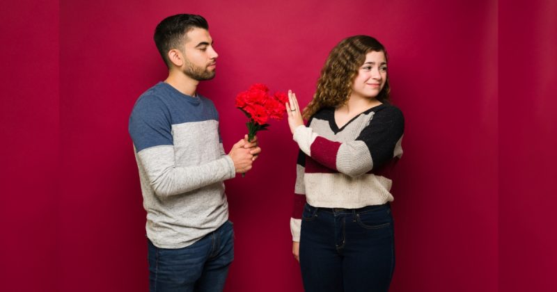 Homem entregando flores a mulher, que por sua vez, recusa