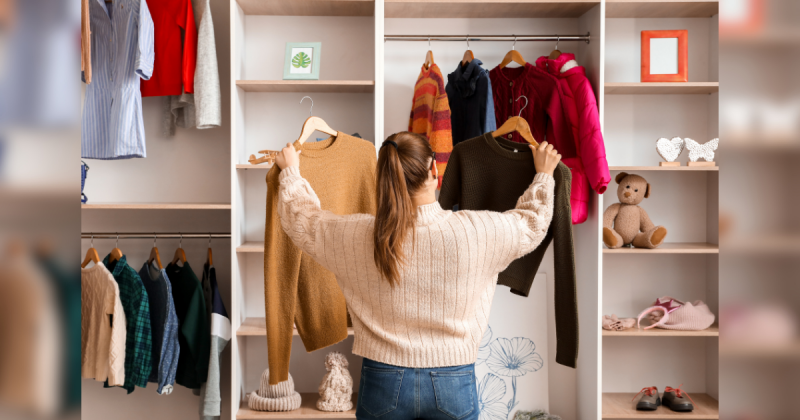 Mulher de costas escolhendo blusa marrom e creme, com um guarda-roupa à frente