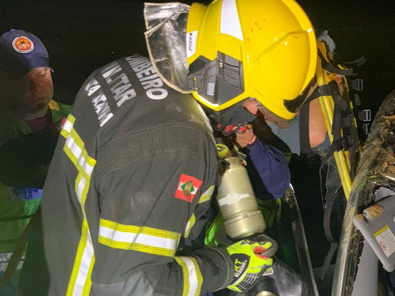 A imagem mostra bombeiros socorrendo homem preso dentro do carro.