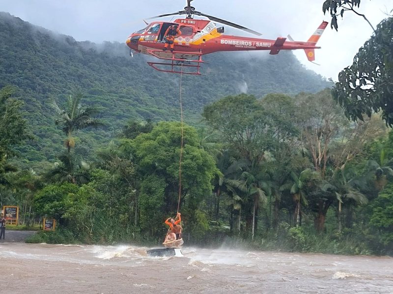 Na foto, dois homens que estavam em cima de um carro quase totalmente submerso ficam pendurados em corda puxada por helicoptério. São homens ilhados em cima de carro durante enxurrada no Norte de SC.