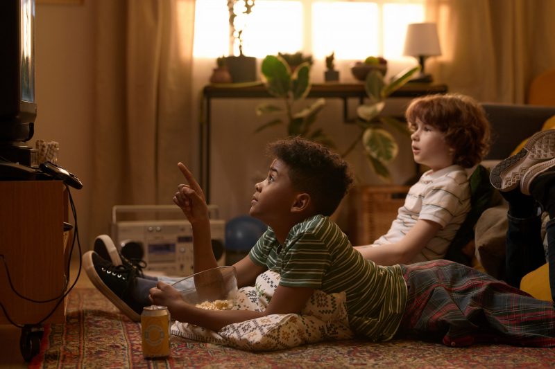 Dois meninos assistindo programa de TV em casa, sentados no chão da sala.