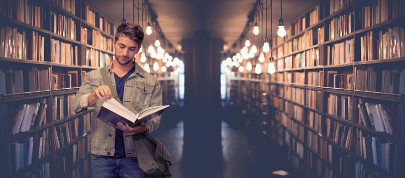 Jovem lendo um livro nos corredores de uma bilbioteca 