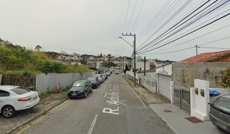 Mulher mata namorado a facadas após discussão na rua Adolfo Donato da Silva, na Praia Comprida, foto mostra rua à luz do dia, carros estão estacionados em uma lateral em uma rua com casas umas ao lado das outras