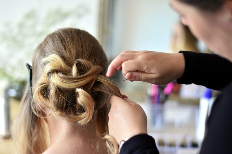 Mulher loira de costas tendo seu cabelo ajeitado no salão de beleza