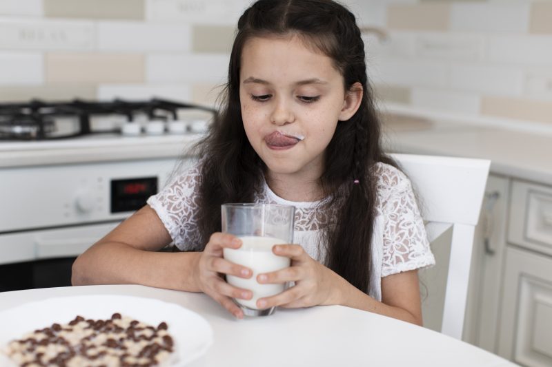 Criança lambendo os lábios tomando leite com suplemento alimentar