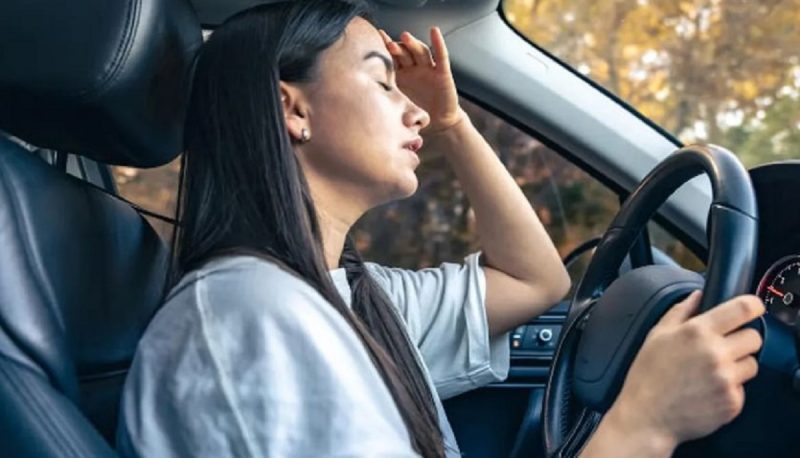 na foto aparece uma mulher sentindo calor por não fazer o truque para baixar a temperatura dentro do carro