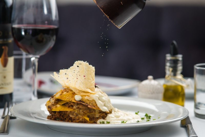 Prato de lasanha com taça de vinho ao fundo 