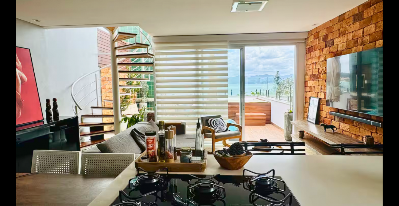 Sala, cozinha e varanda com jacuzzi têm vista para o mar neste apartamento - Airbnb/Divulgação