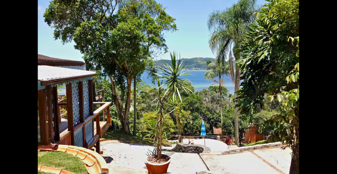 Vista do pátio da casa, cercada pela vegetação, para a Lagoa da Conceição e os morros verdes - Airbnb/Divulgação