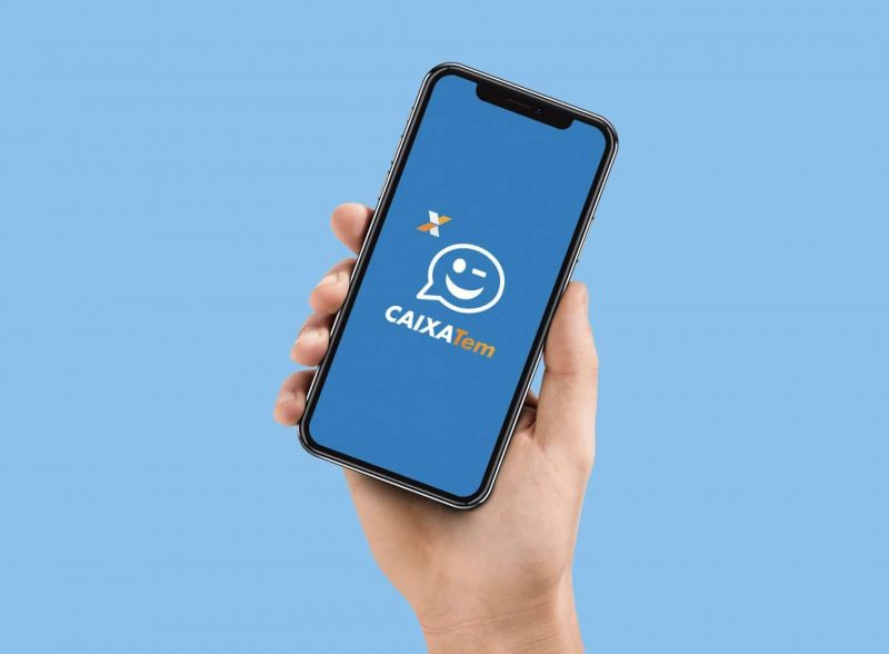 Mão segurando um celular com a tela aberta na página inicial do app Caixa Tem 