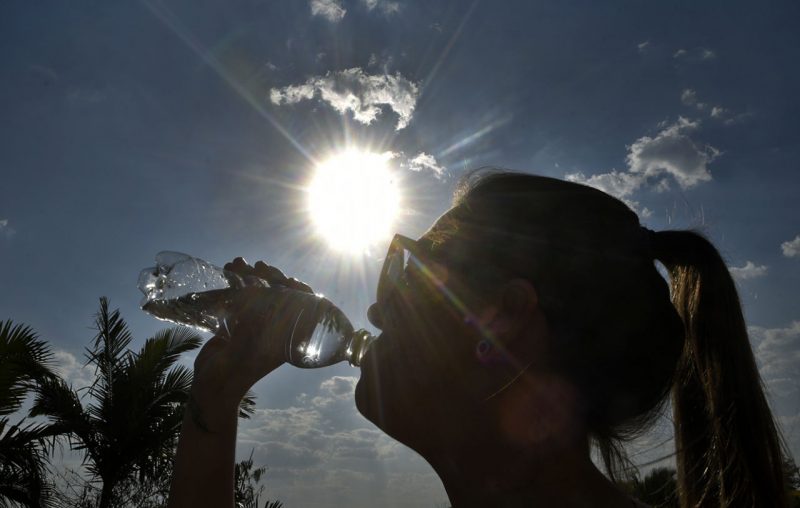 foto mostra mulher tomando água com sol ao fundo, sensação térmica pode chegar a 45°C em SC