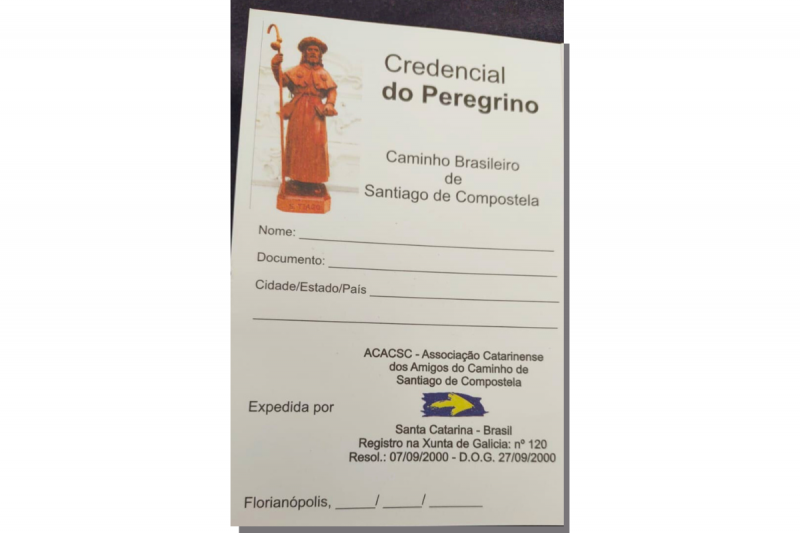 Pequeno cartão com o título: Credencial do Peregrino - Caminho Brasileiro de Santiago de Compostela. Abaixo, campos em branco para preenchimento de nome, documento, cidade, estado e país. A seguir, o carimbo da Associação Catarinense dos Amigos do Caminho de Santiago de Compostela. 