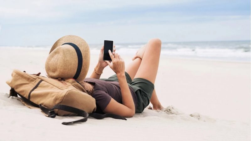 Mulher mexendo no celular na praia, precisando de um verão digital detox