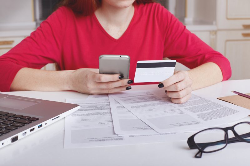 Mulher com cartão de credito em mãos e celular, consultando contas e boletos