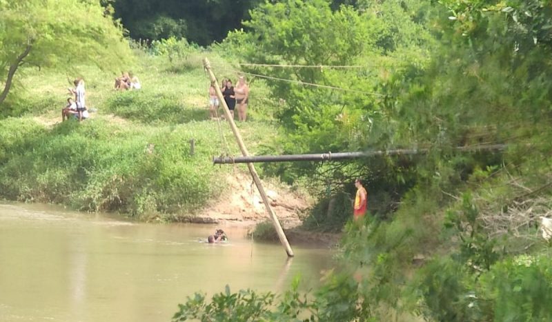 Corpo de adolescente que se afogou ao nadar com o irmão é encontrado em SC, foto mostra bombeiros em rio enquanto pessoas olham da margem