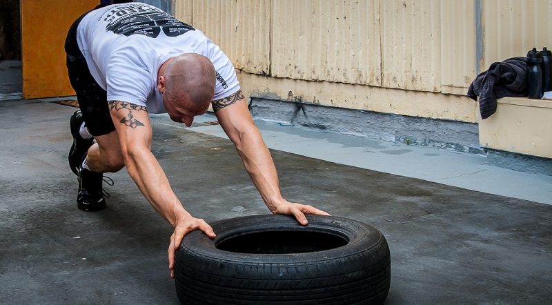 homem inclinado empurrando pneu em aula de crossfit