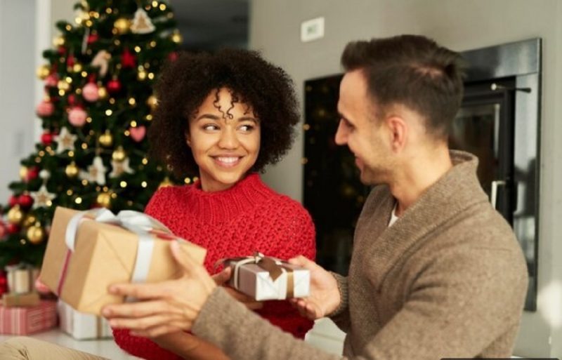 na imagem aparece uma mulher que sorri ao dar presentes de Natal