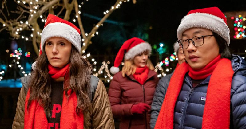 Um casal com cara emburrada vestidos com roupas de natal em frente a árvores de natal 