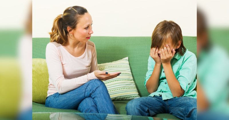 Mulher conversando com menino que está com mãos no rosto