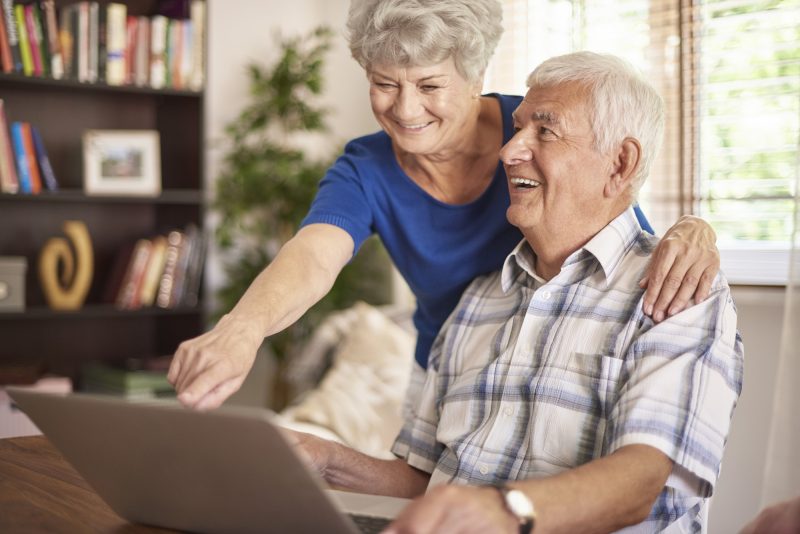 Casal de idosos sorrindo sentados em frente ao notebook 