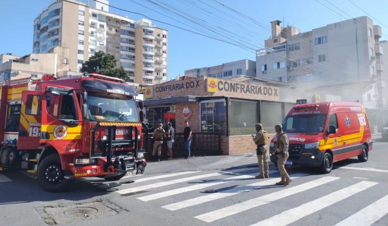 Incêndio em lanchonete de Florianópolis, foto mostra fumaça saindo de lanchonete, pessoas na frente e um caminhão e ambulância dos bombeiros