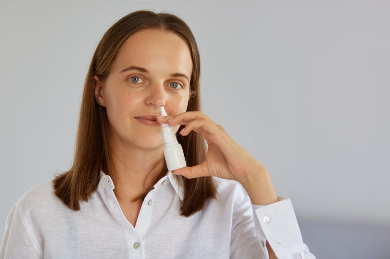 Mulher com leve sorriso segurando um spray nasal próximo ao nariz 