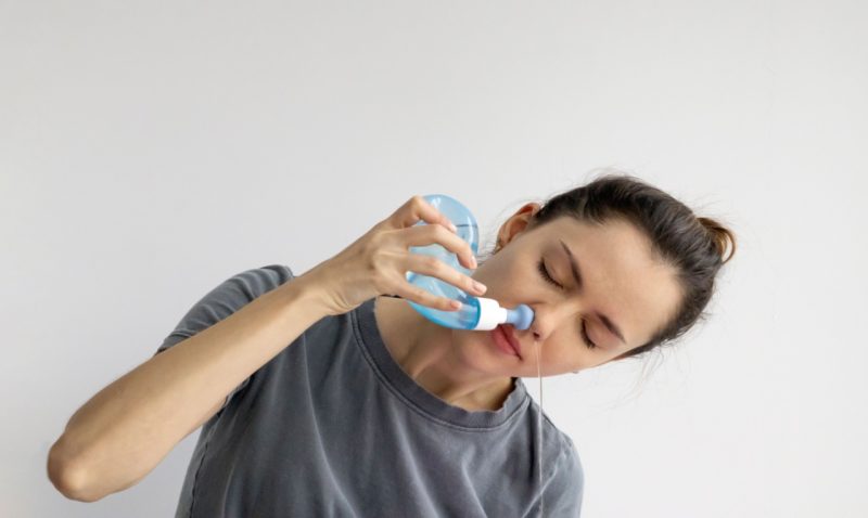 mulher inclinada usando a lota nasal para fazer a lavagem nasal