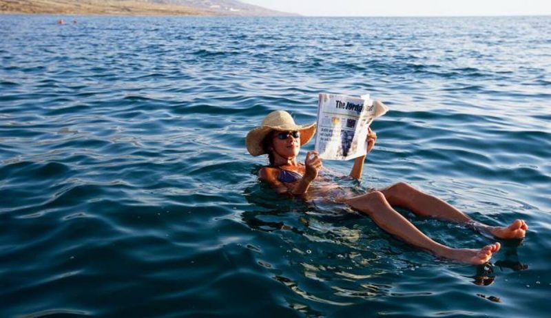 Mulher lendo jornal enquanto boia no Mar Morto