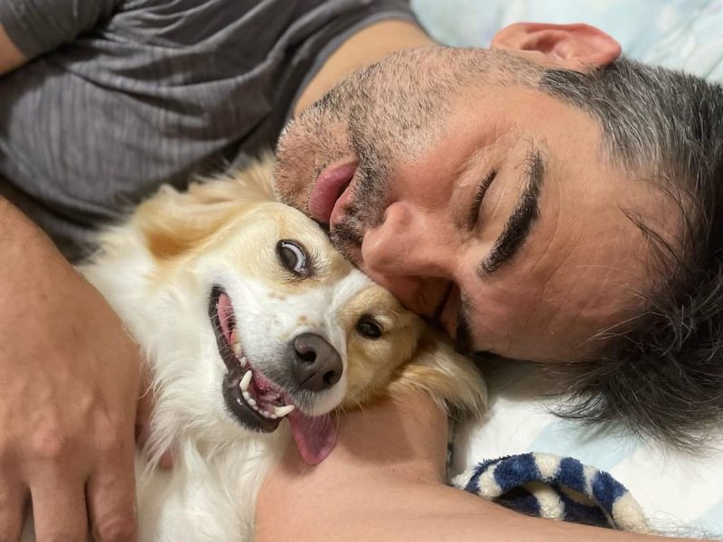 A imagem mostra o tutor e a cachorrinha chamada Mel - cachorra que ele pensou que fosse uma vira-lata - abraçados na cama. 