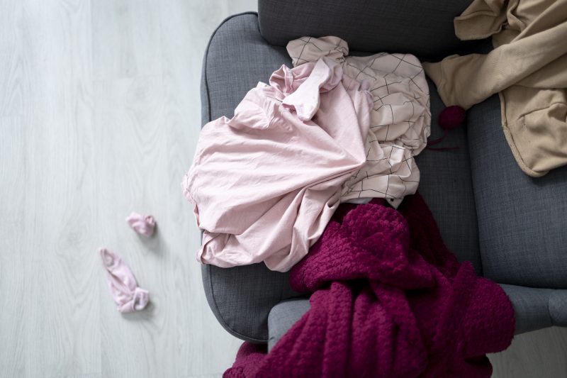 Sofá bagunçado com roupas sobre ele 