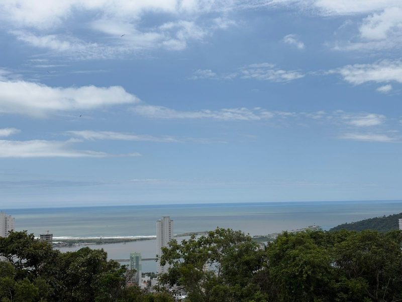 Foto da paisagem de Itajaí com árvores, céu azul e vista para o mar. Pancadas de chuva no Litoral Norte de SC. 