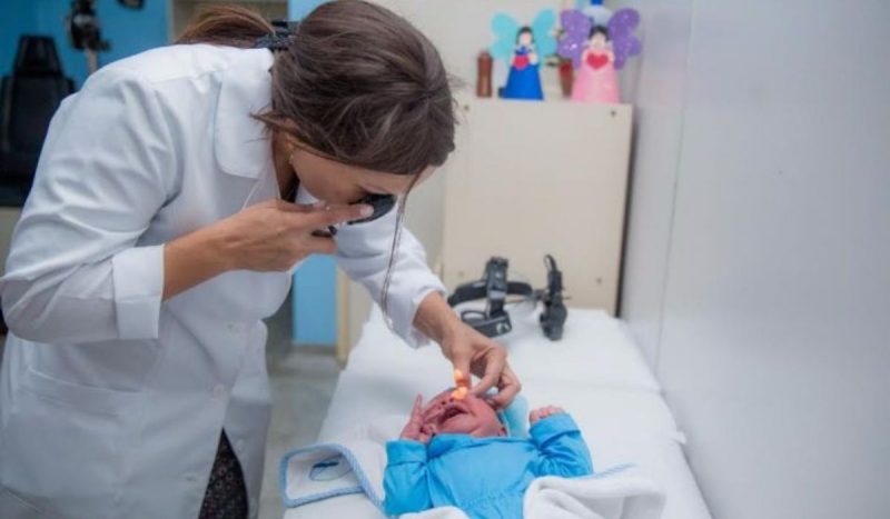 médica realizando teste do olhinho em recém-nascido deitado em maca de hospital