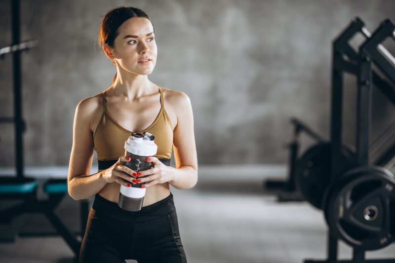 Mulher segurando garrafinha de água com whey na academia 