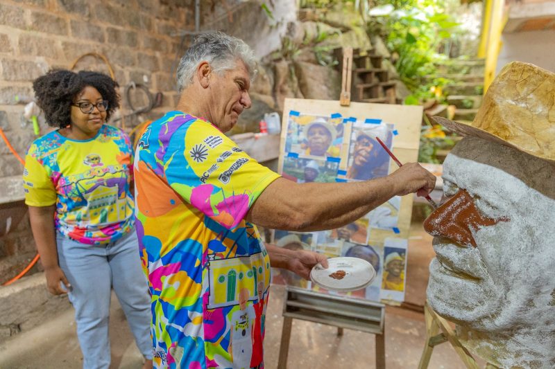 Artista Allan Cardoso usa fotos de diferentes ângulos para moldar o rosto de Seu Lidinho, sob o olhar atento da neta do passista, Luiza Nunes Costa 