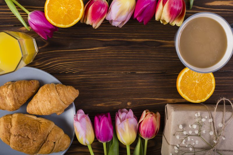 Fundo de mesa de madeira decorada com flores e frutas, xícara de café e croassants 