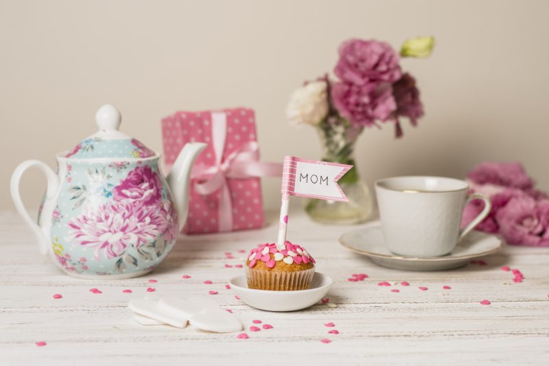 Mesa de café da manhã de aniversário, com um cupcake decorado, flores, bules e xícaras no tom rosa e branco 