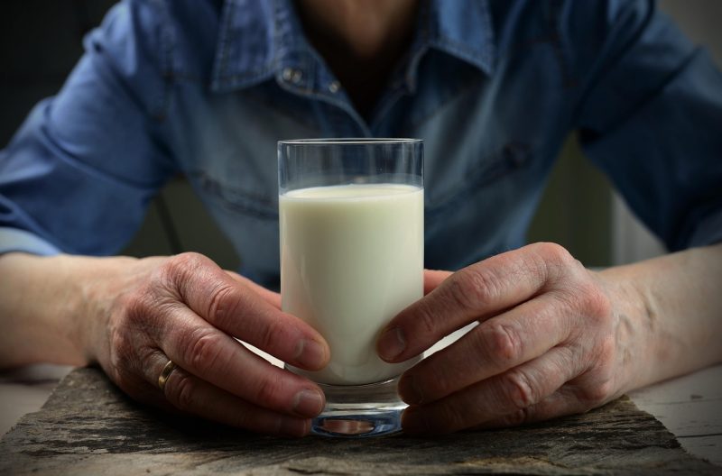 Imagem com foco nas mãos de um homem, segurando copo de leite, alimento com muito cálcio 