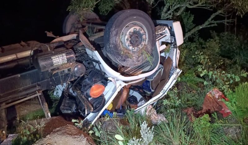 Motorista foi encontrado fora do caminhão, em estado grave, foto mostra caminhão tombado com todas pra cima em área de mata