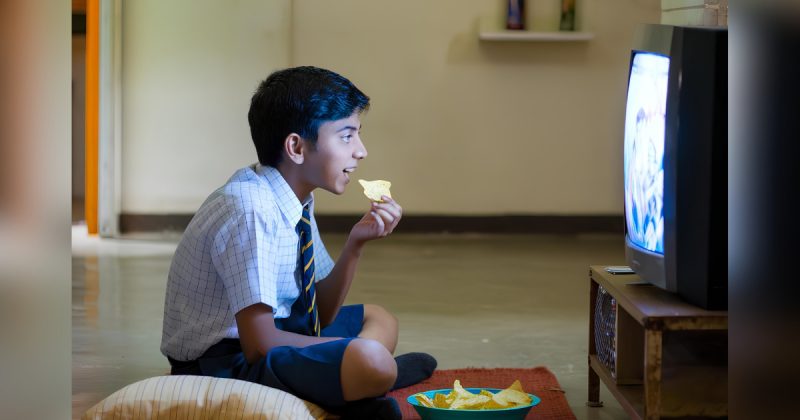 Menino comendo comida na frente de televisão