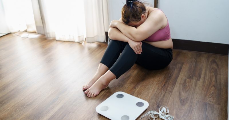 Pessoa sentada no chão com braços pela perna e pela cabeça