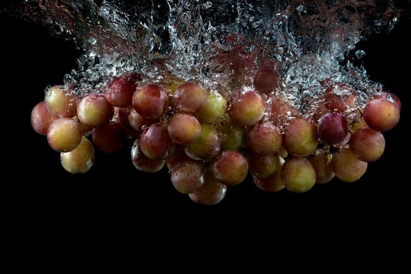 Uvas sendo despejadas na água em um fundo preto