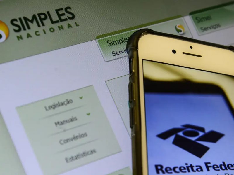 Celular com tela no site da receita federal frente ao site do simples nacional no desktop 