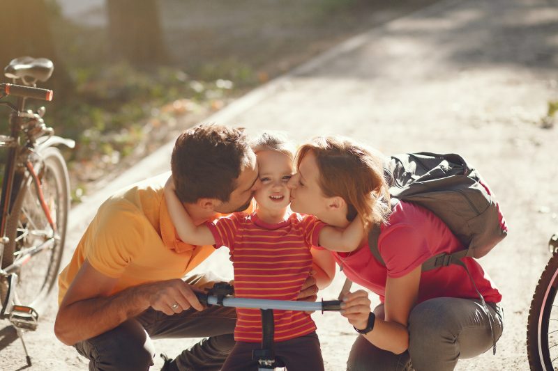 Pais com sua filha em um parque andando de bicicleta